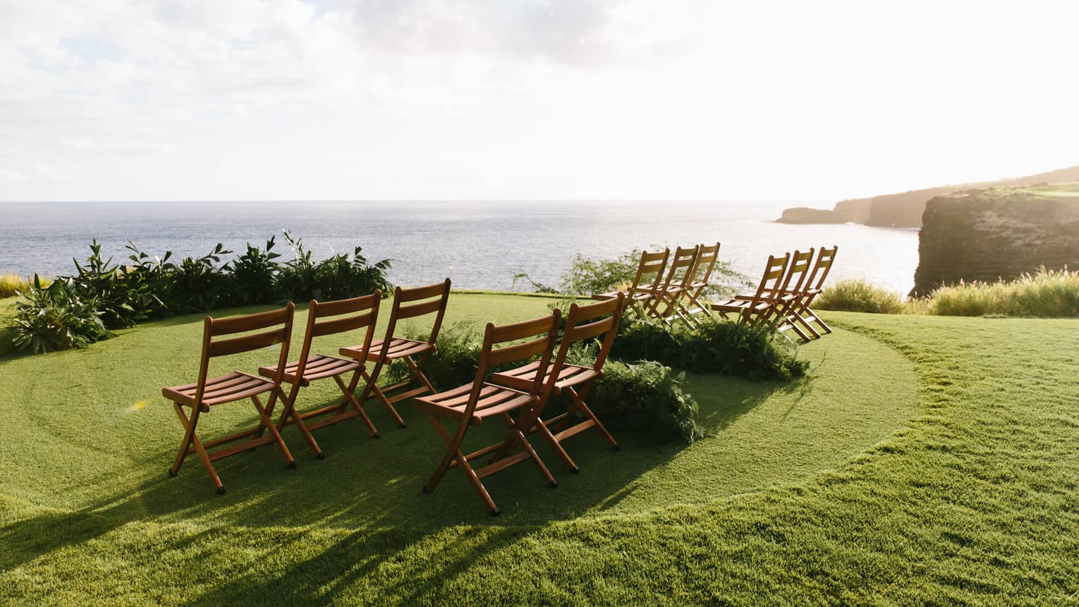 A series of wooden chairs set up on a golf course overlooking a calm sea.