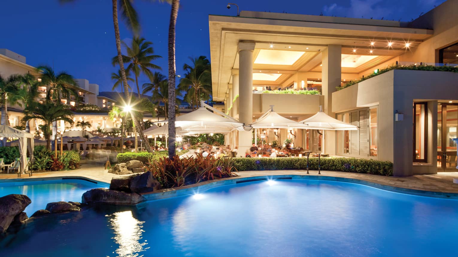 Guests dining beside the Keiki Pool, illuminated at night 