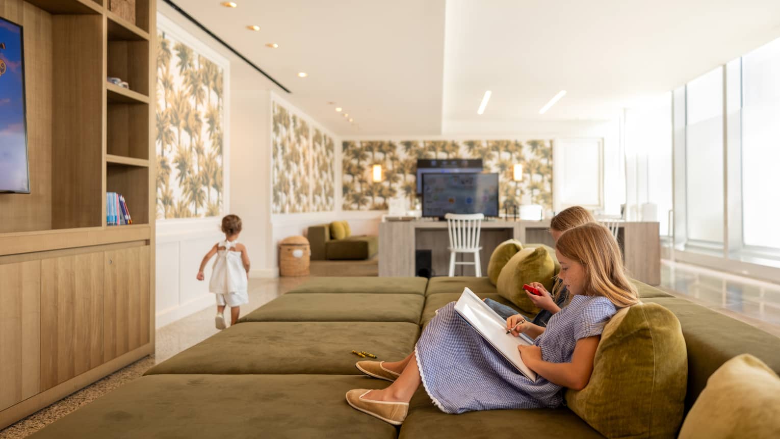 Children watch TV and read books on large sofa in kids club at luxury hotel