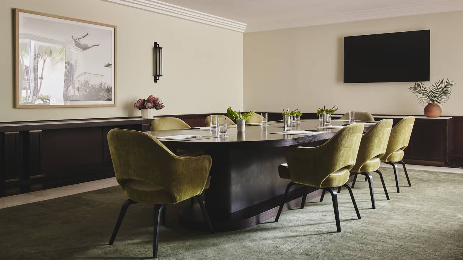 A boardroom with a large table and suede chairs surrounding it, a tv hanging on a wall and counters wrap around the room.