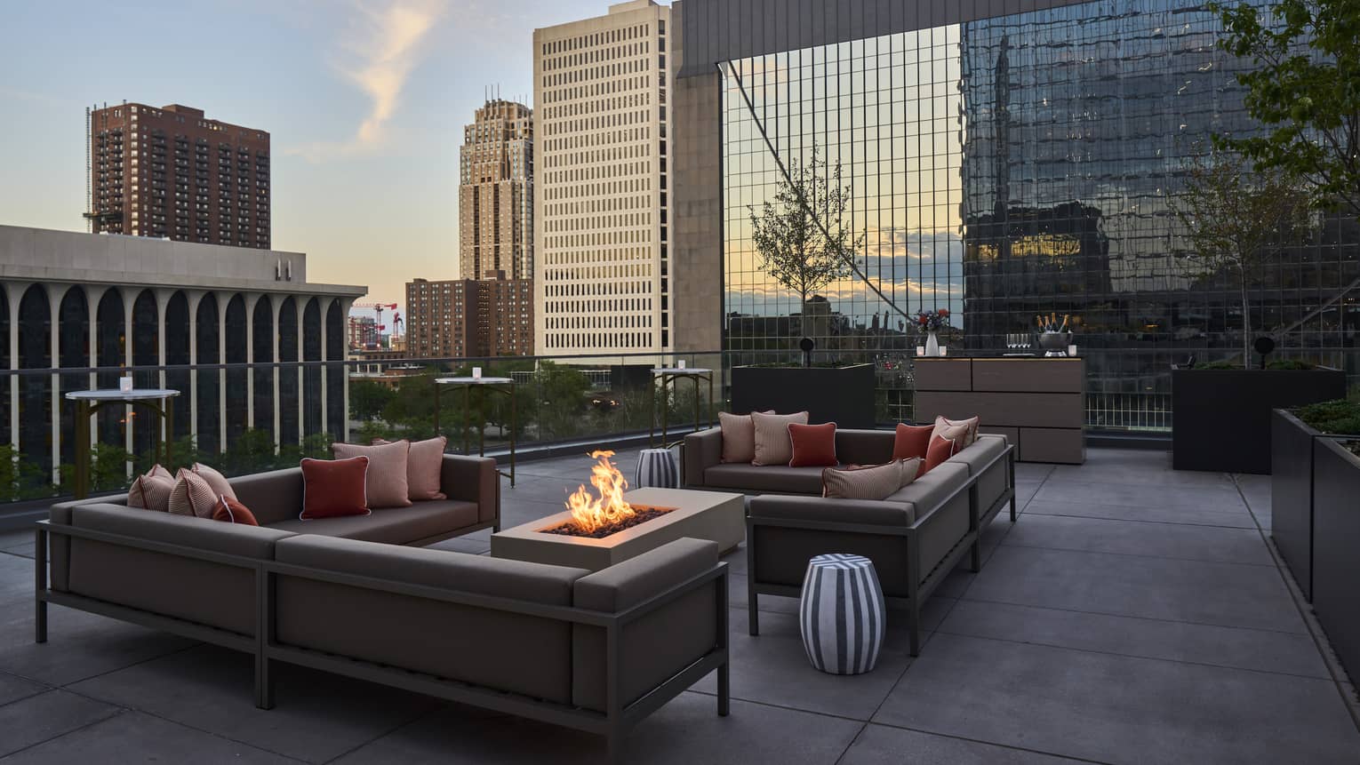 A seating area on a terrace with a fire pit, couches and small tables.