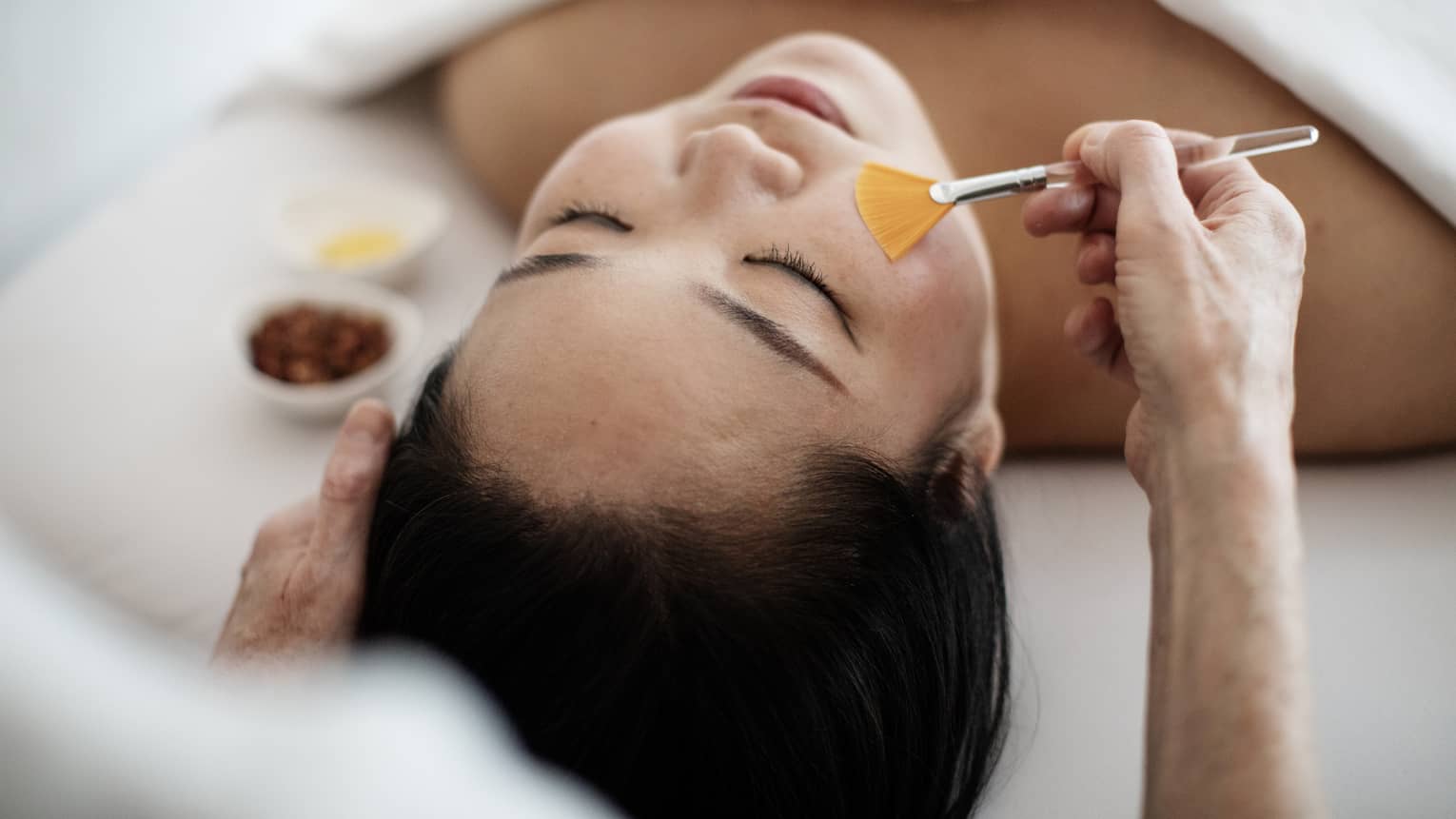 A woman receiving a spa treatment utilizing a brush on her face.
