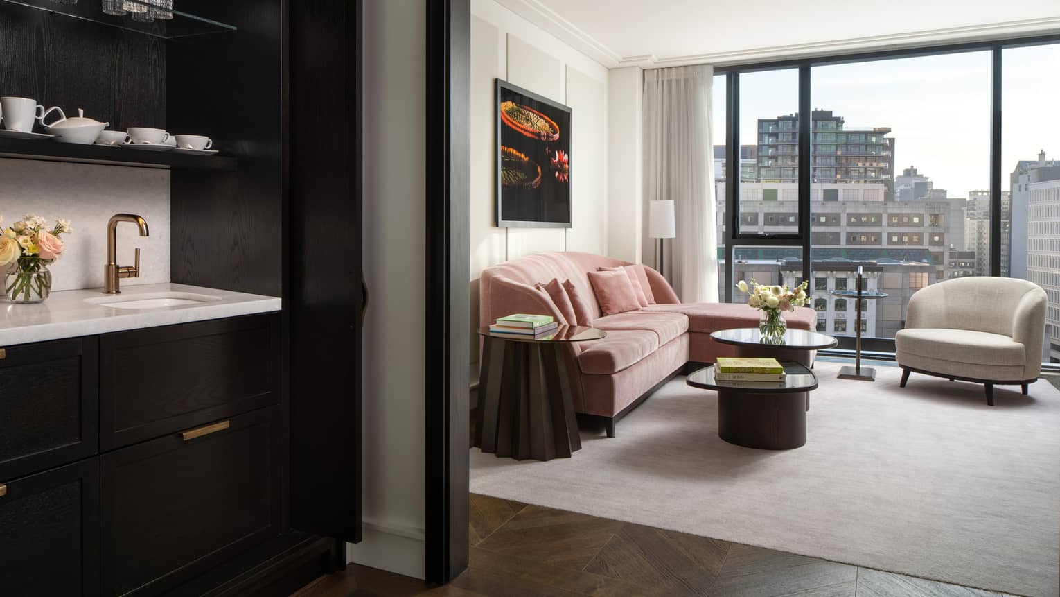 Hotel room living area with pink velvet sofa, ivory arm chair and wall of windows