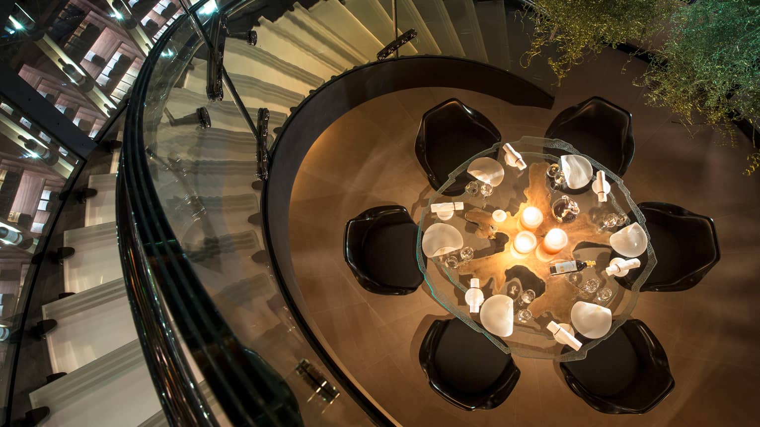 Aerial view of round glass candle-lit dining table, chairs from spiral staircase