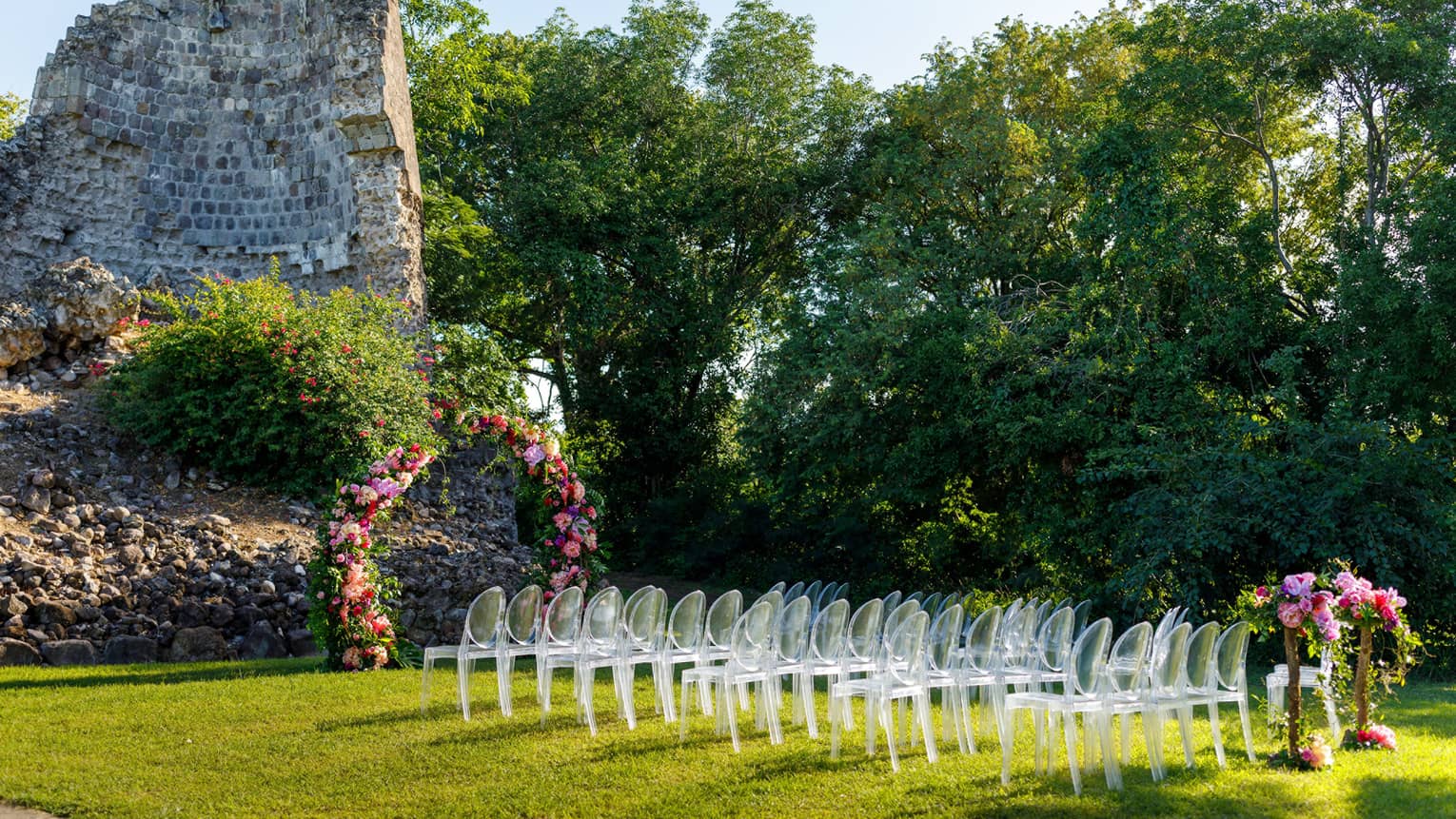 Outdoor wedding setup at Tea Mill rock structure, lucite chair grouping, flowers, flanked by bushes
