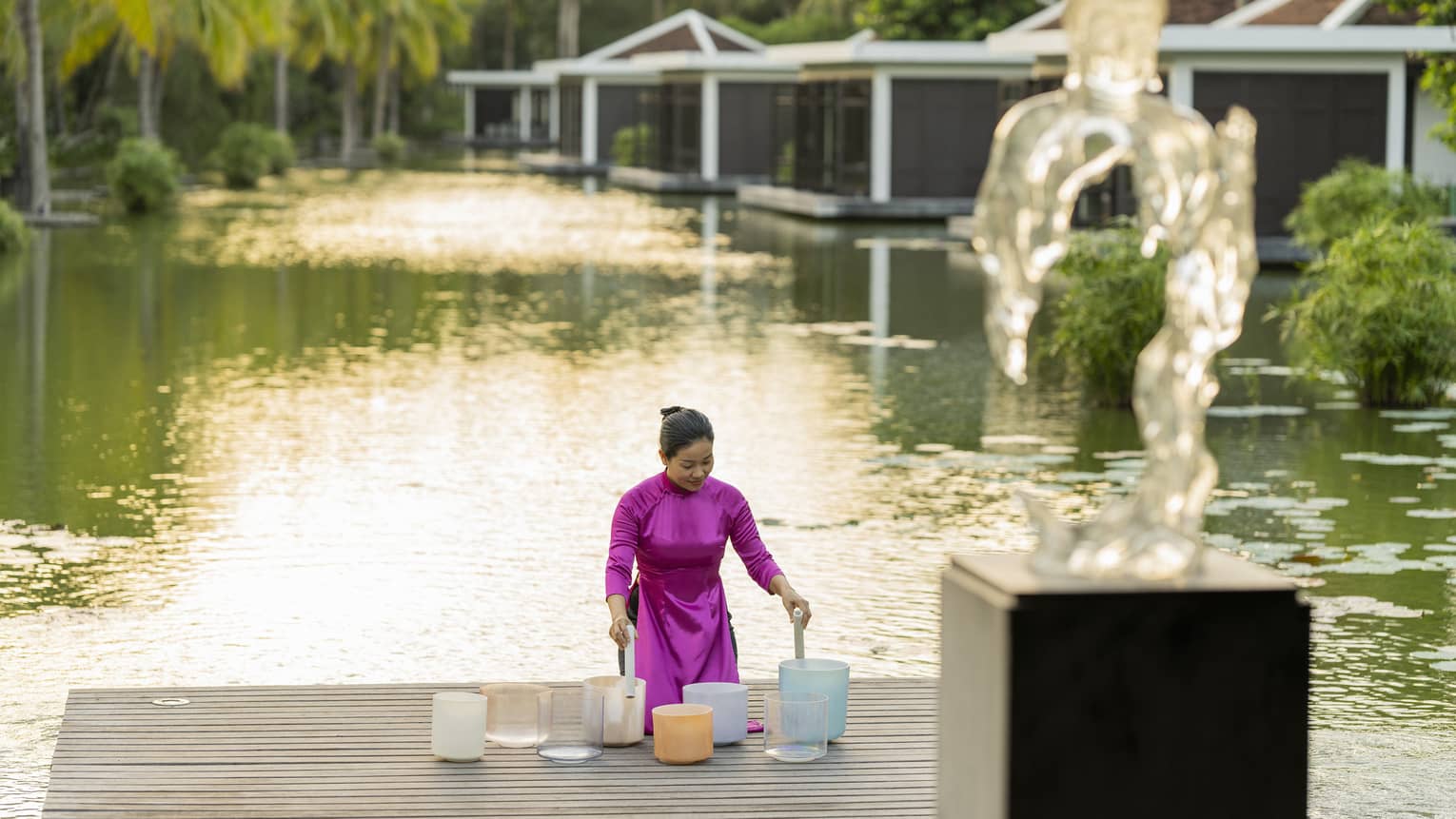 Woman plays crystal singing bowls on the dock of the lake