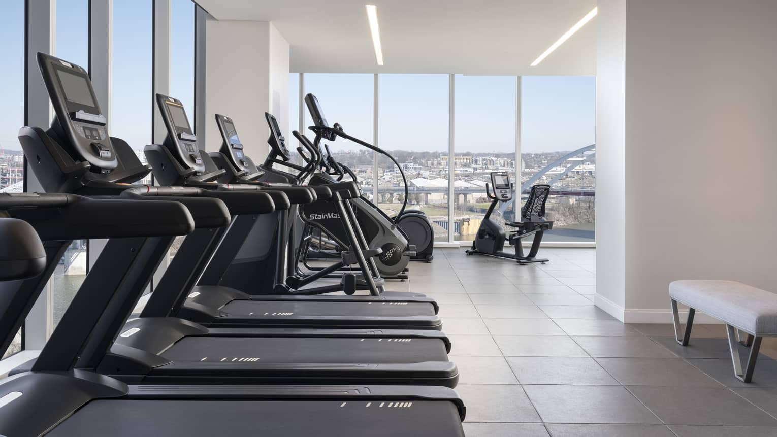 A fitness centre with cardio machines and large windows.