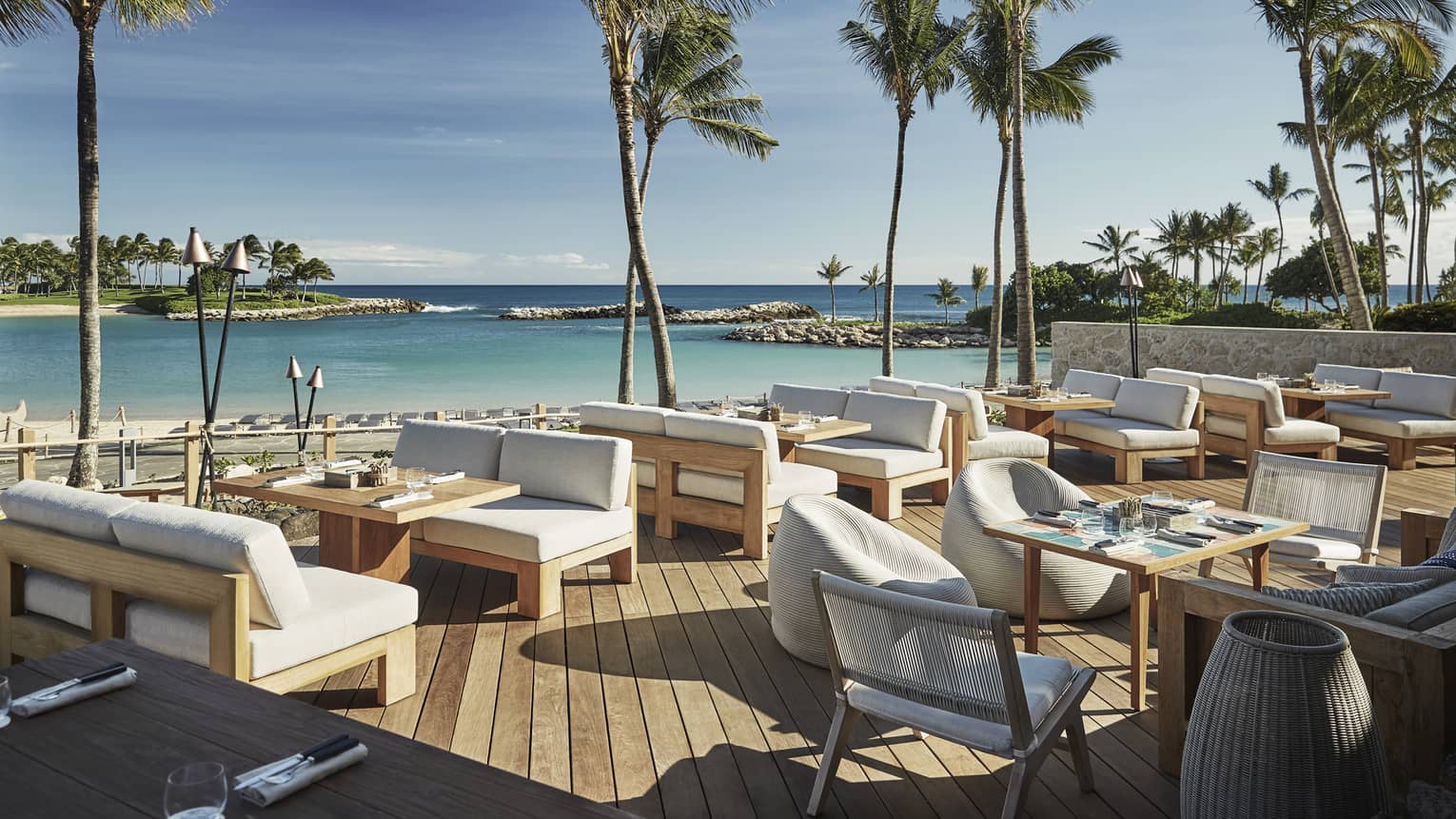 Plush white patio chairs around wood tables on sunny waterside Minas lounge