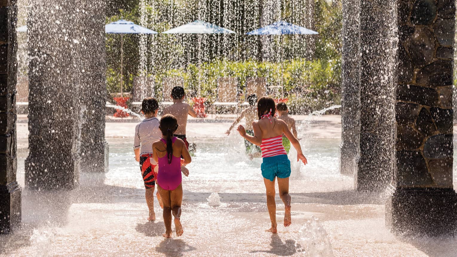 Children run past pillars, splash under falling water on Splash Zone water park