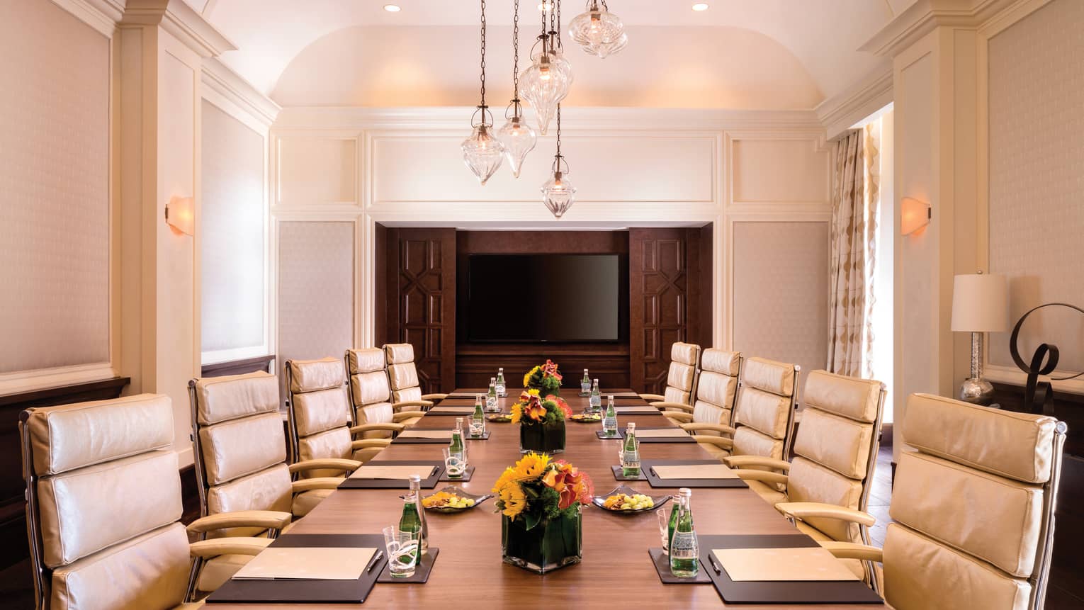 Executive Boardroom with large meeting table set with agendas and flowers, lined with tan leather chairs 