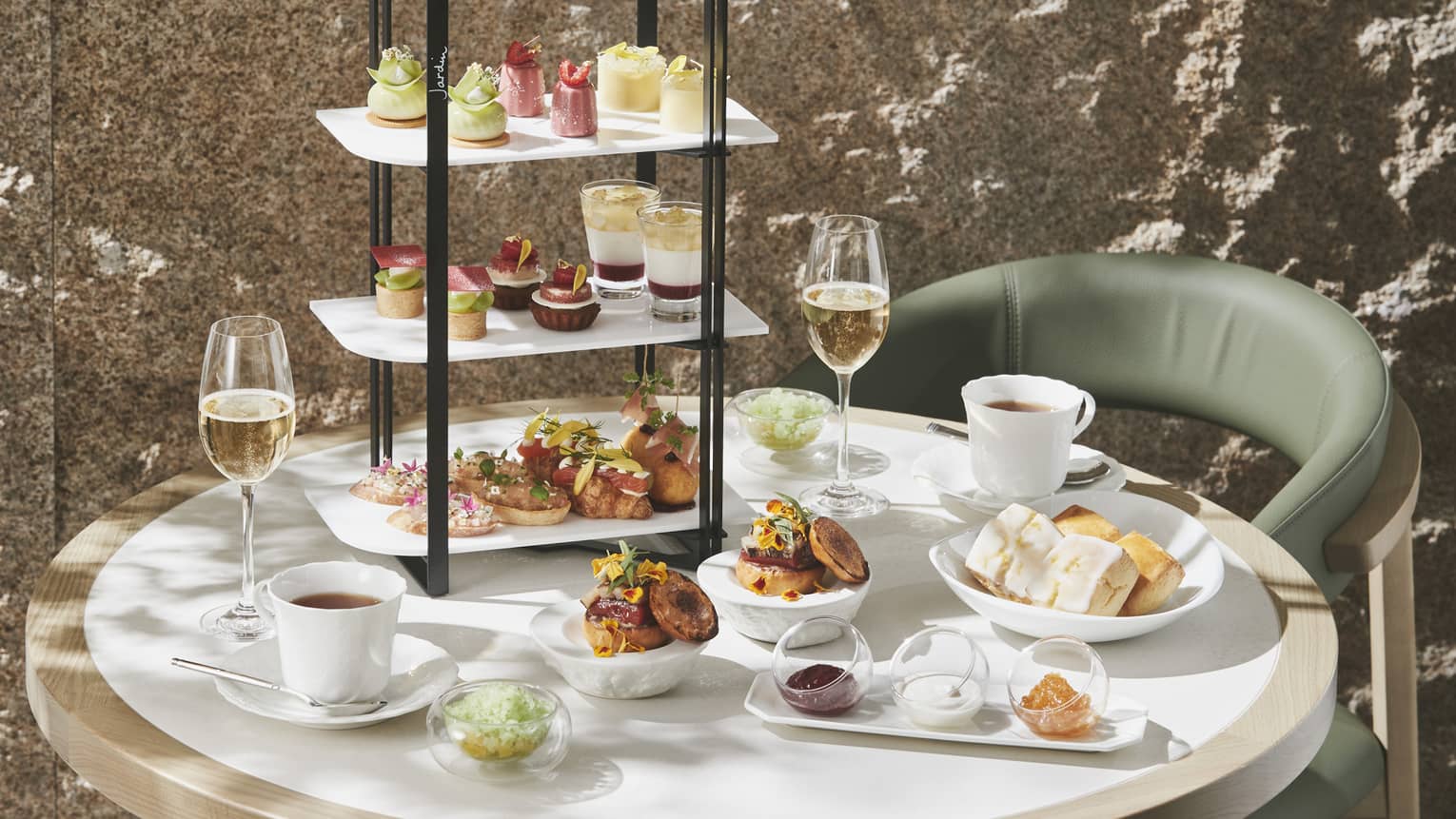 Afternoon Tea set up with three-tiered display of sweet and savoury foods, two glasses of champagne and two glasses of tea