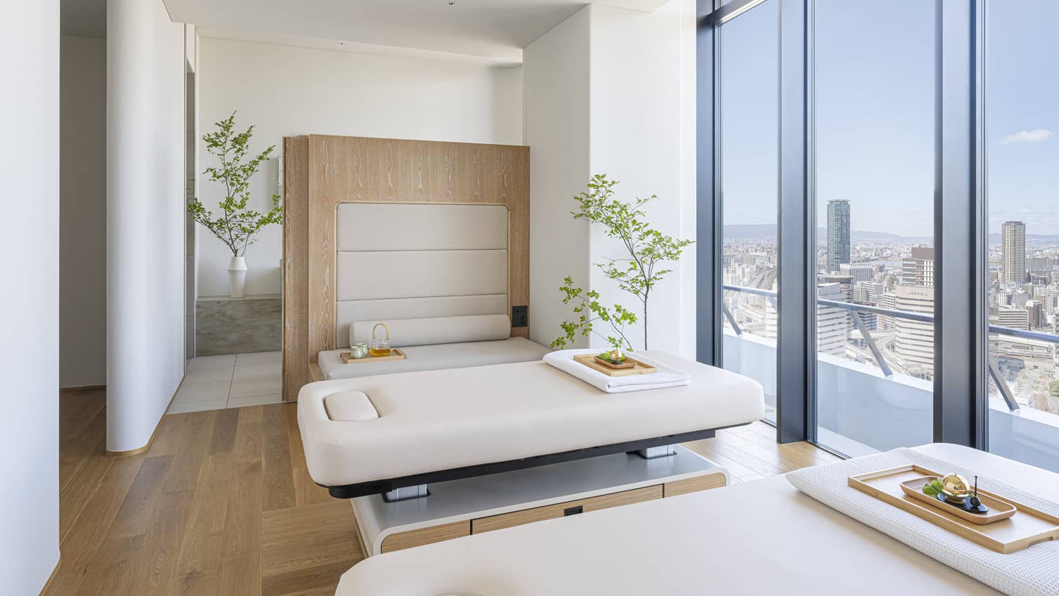 Spa treatment room with two treatment tables and wall of windows overlooking city at The Spa at Four Seasons Hotel Osaka