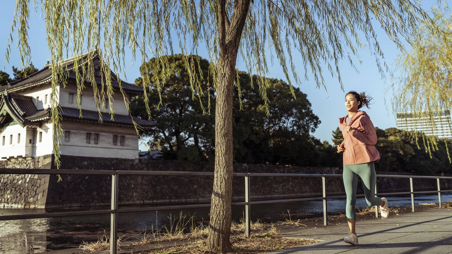 Woman jogs by Japanese temple and moat