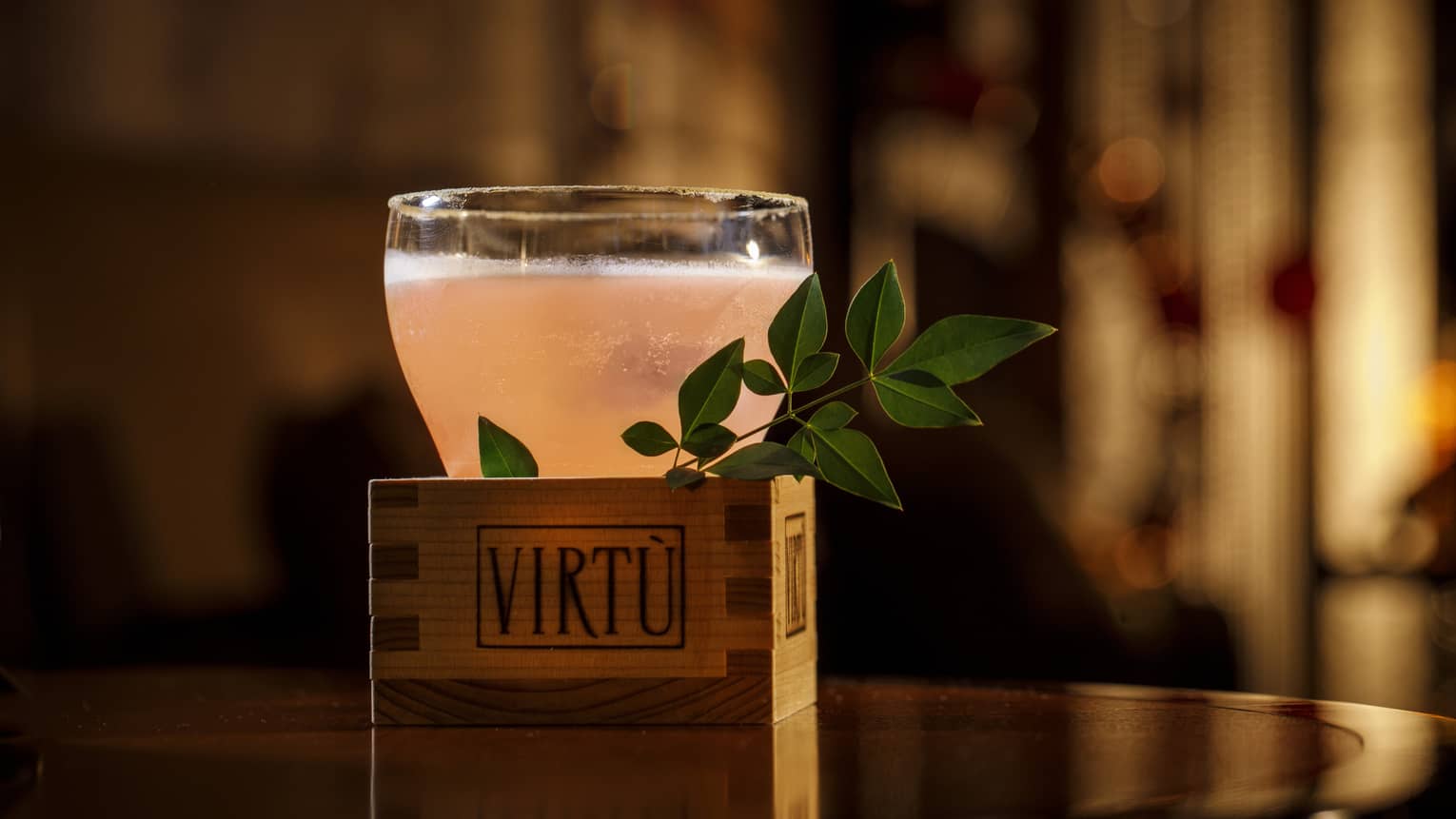 Pink-hued cocktail in wooden VIRT� box with herb sprig