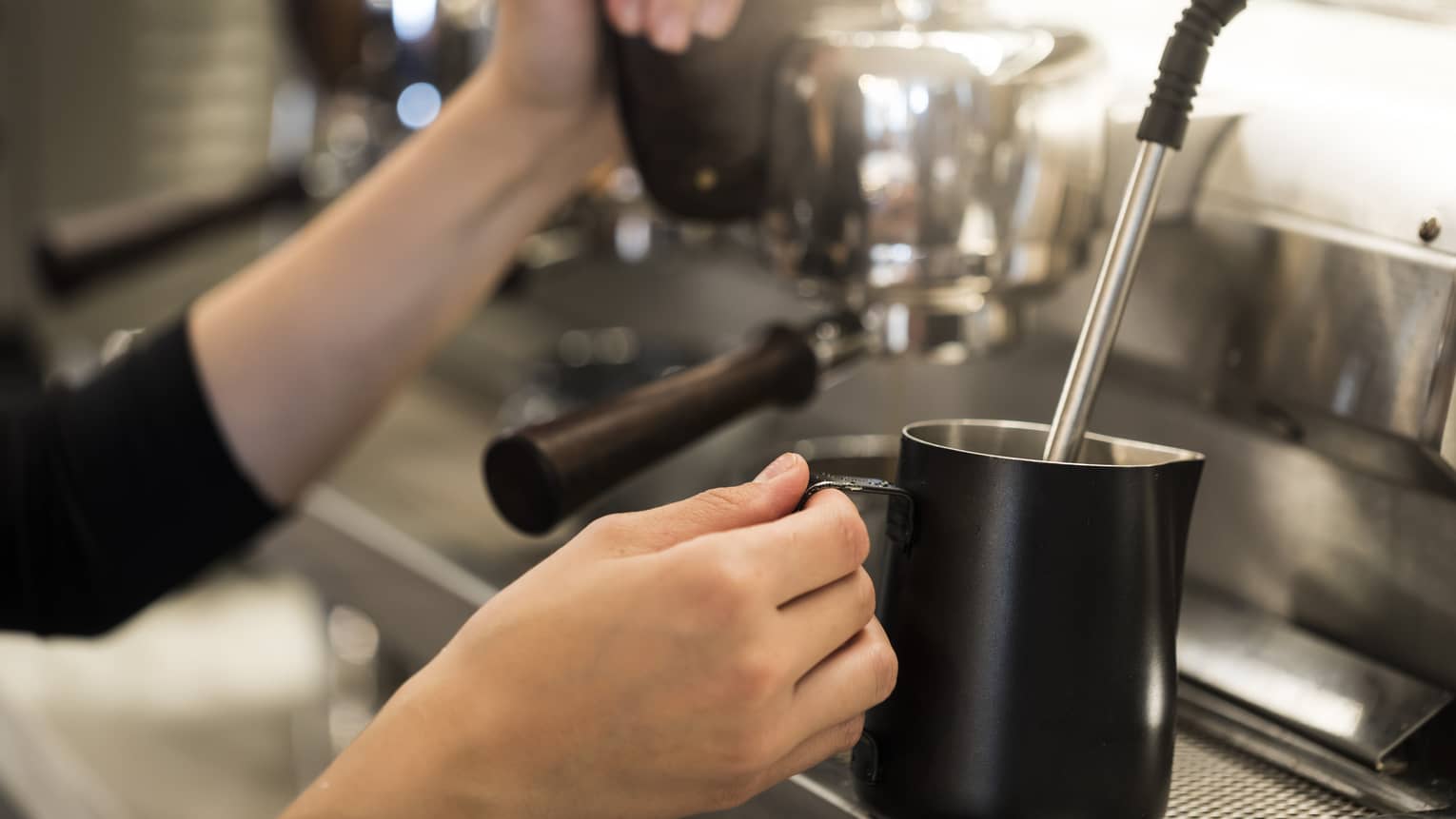 Close-up of hands with milk steamer at espresso machine