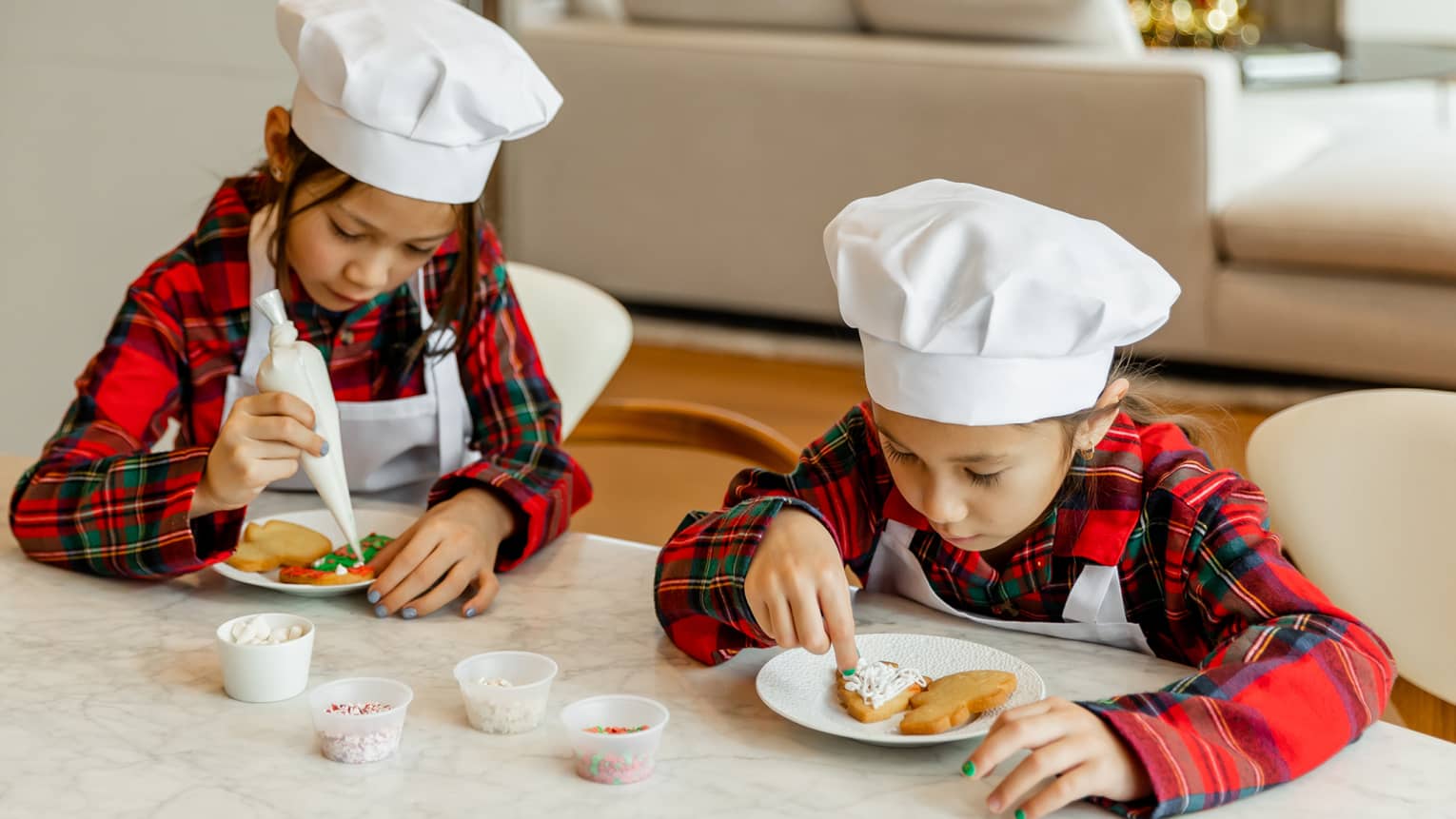 Two children wearing chef hats and decorating cookies.