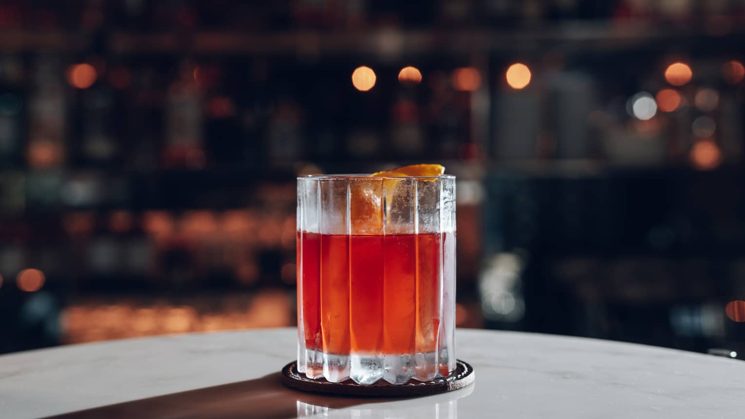 Amber-coloured Negroni cocktail in old fashioned glass with orange peel garnish on marble table