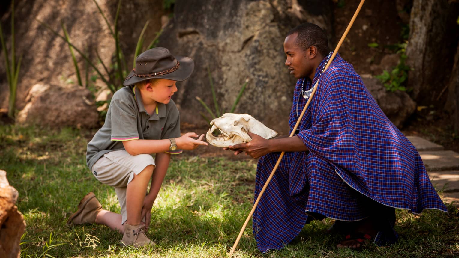 Maasai guide shows large skull to young boy wearing safari hat