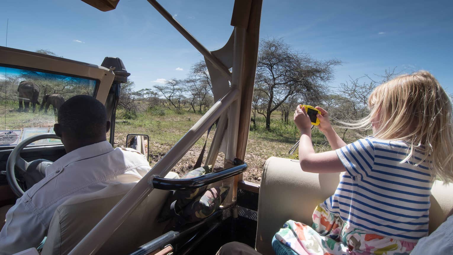 Young girl takes photos of elephants from backseat of safari Jeep