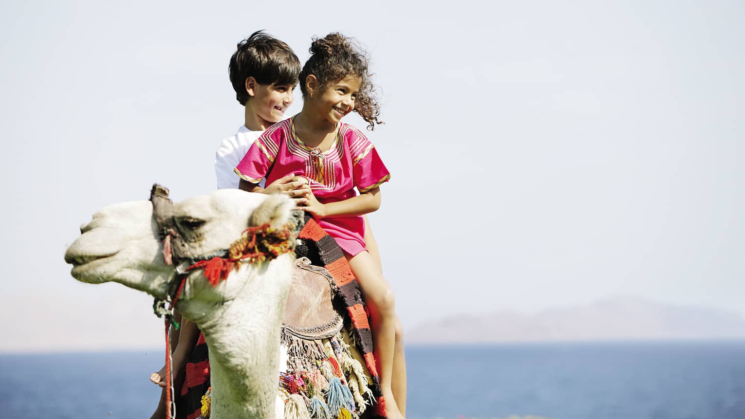Two smiling children riding on camel