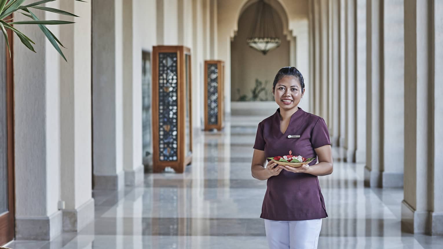 Smiling spa staff member standing in high-ceilinged hallway filled with natural light