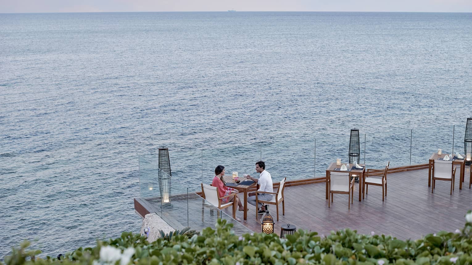 Couple at patio dining table on deck overlooking water