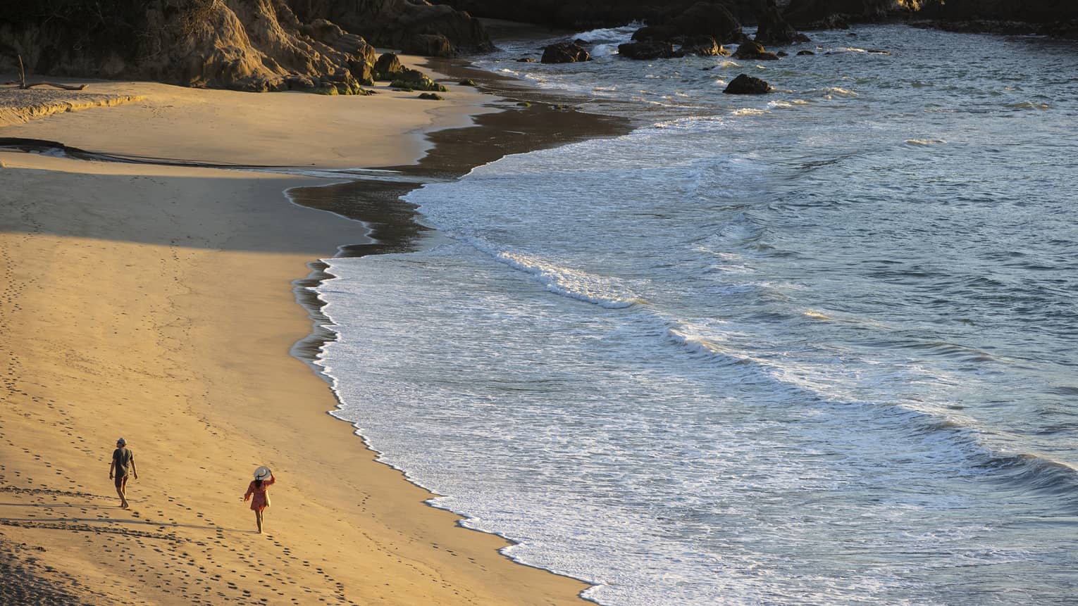 Two people walking along a beach shore.