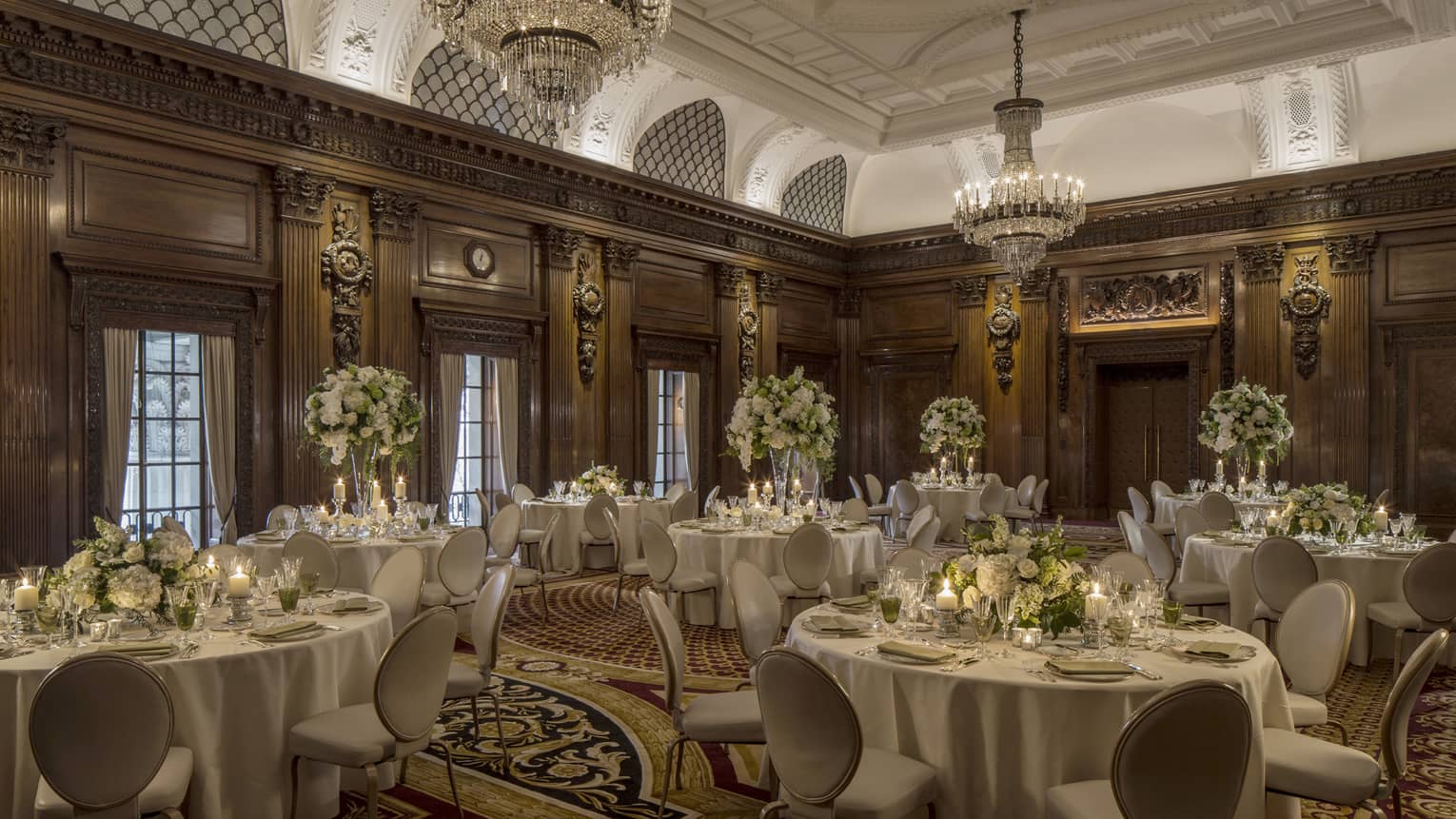 Elegant ballroom with decorative wood walls, crystal chandeliers over round banquet dining tables