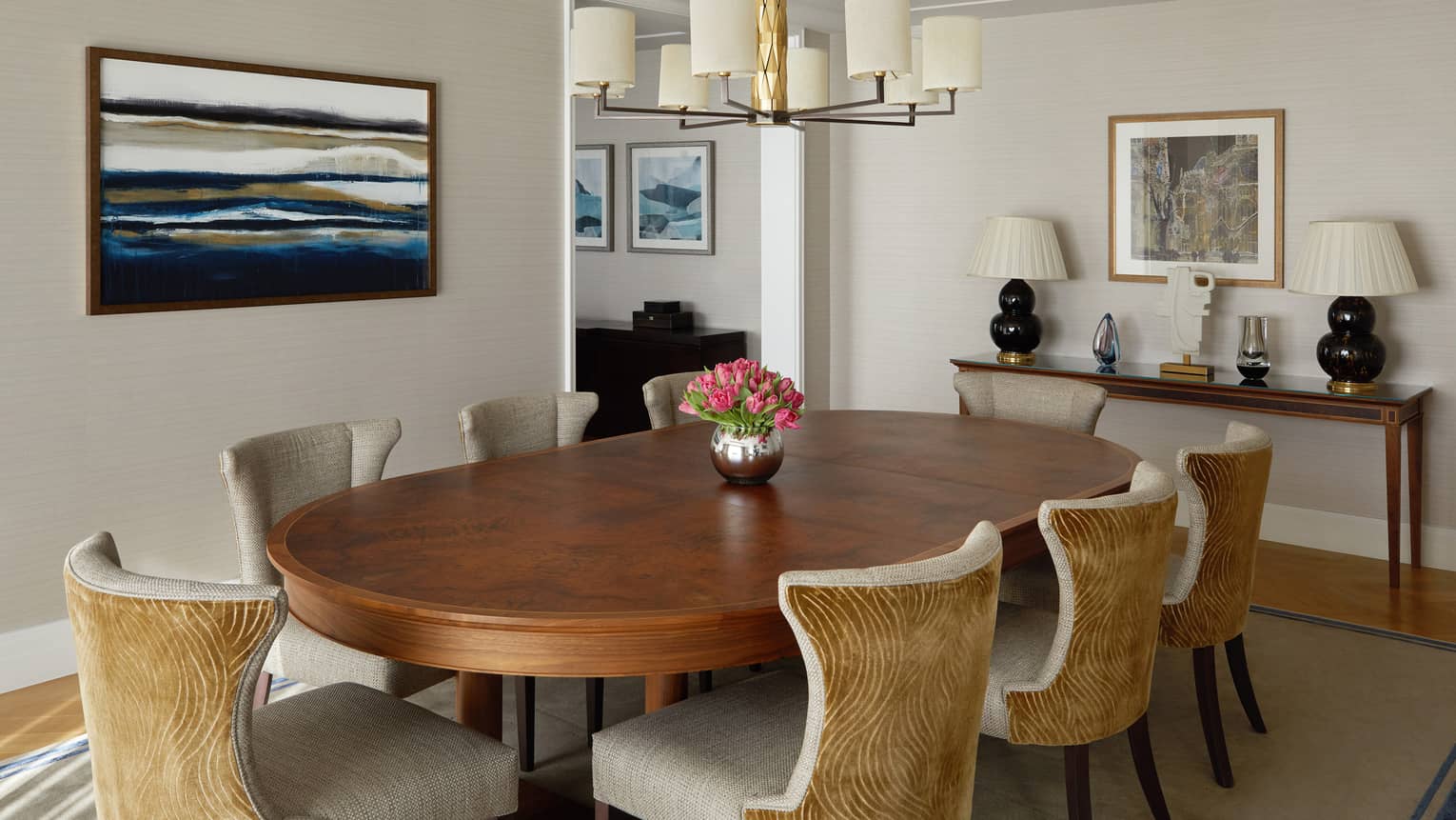 A dining area with large wood table, hanging light, art on the walls and a shelf.