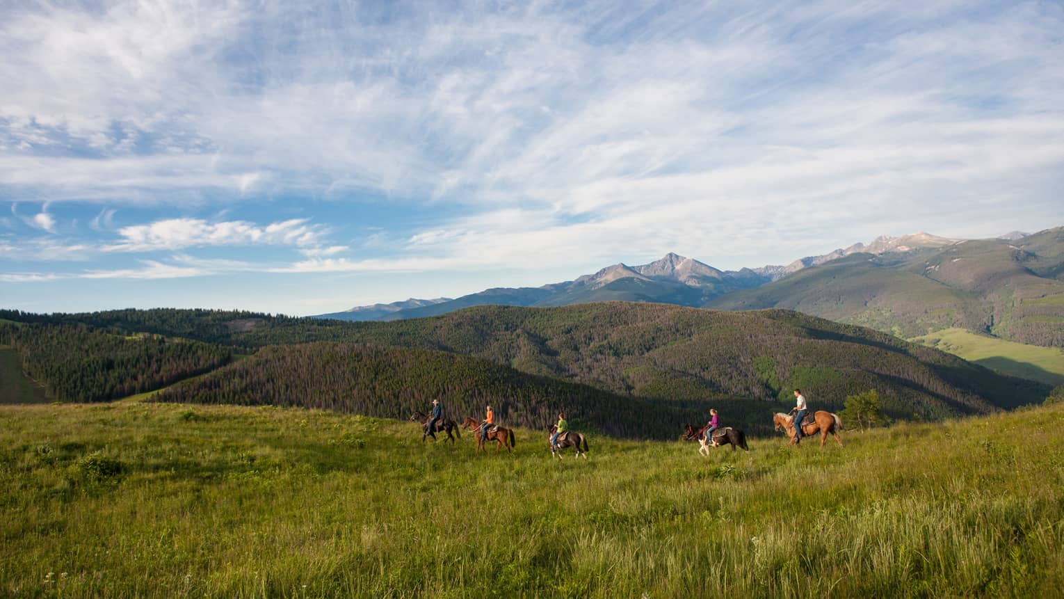 A group of people on horseback riding along grass and hills.