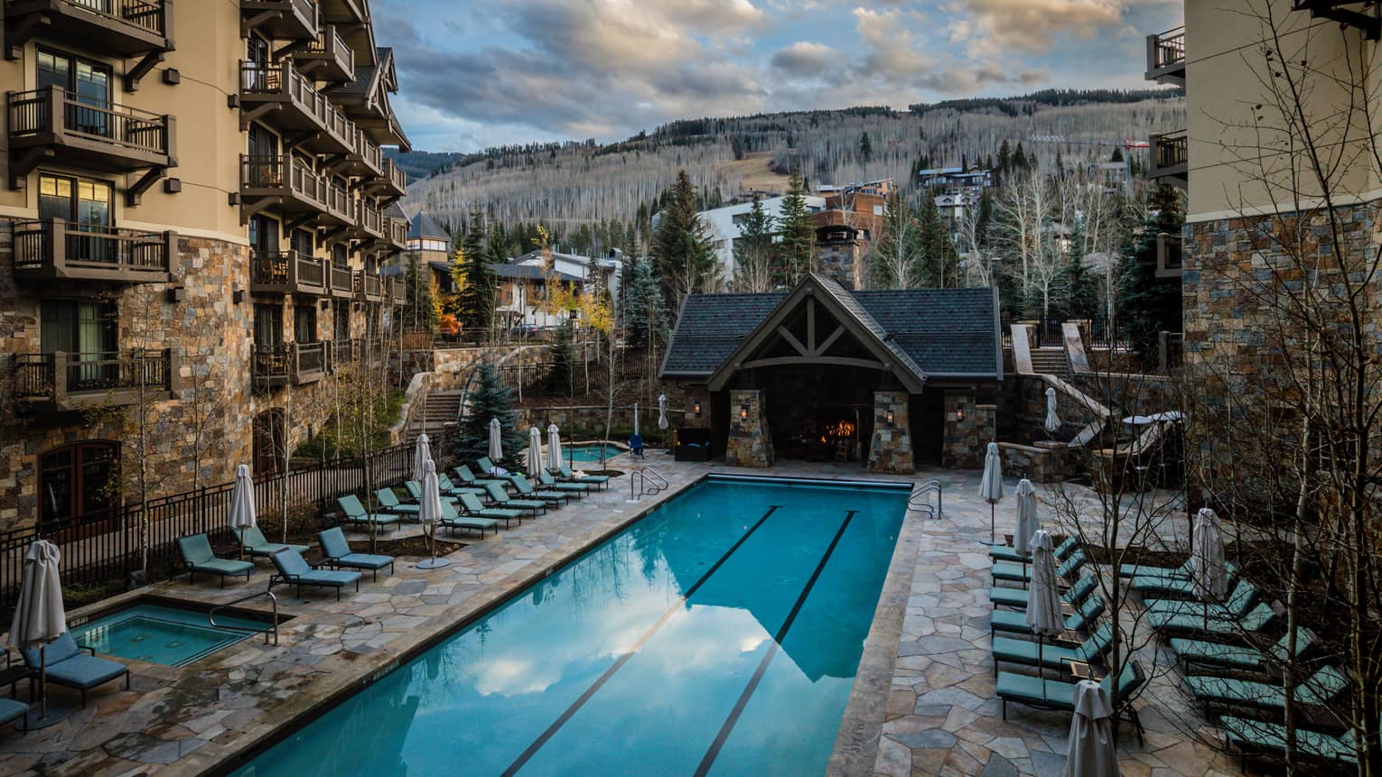 Blue lounge chairs face rectangle heated pool, surrounded by hotel building and mountain views