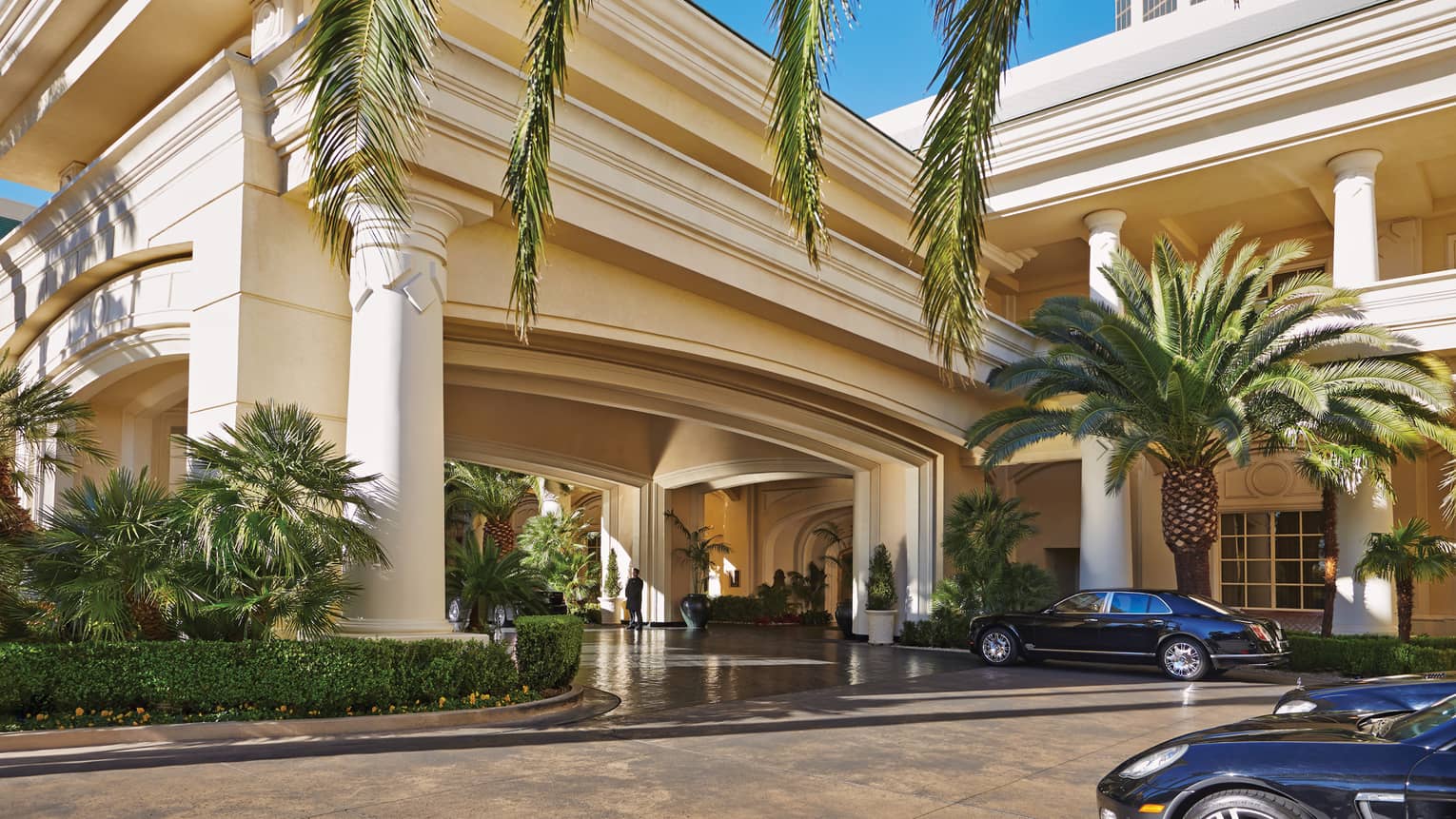 Luxury car parked by palm tree, large white pillars and front hotel entrance
