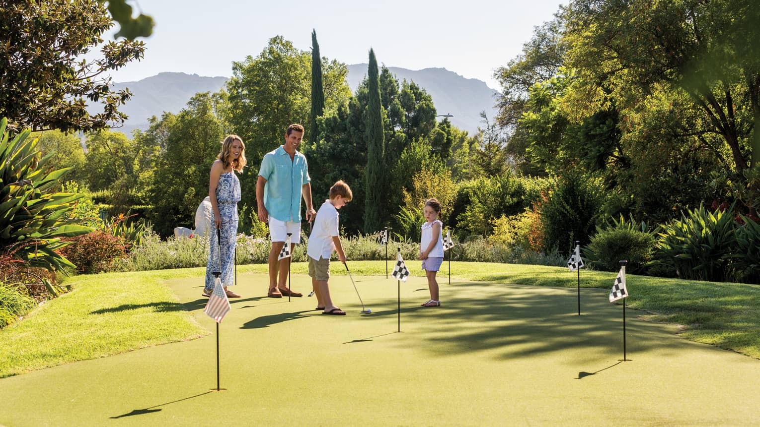 Young boy prepares to putt on mini putting green with flags as sister, parents watch