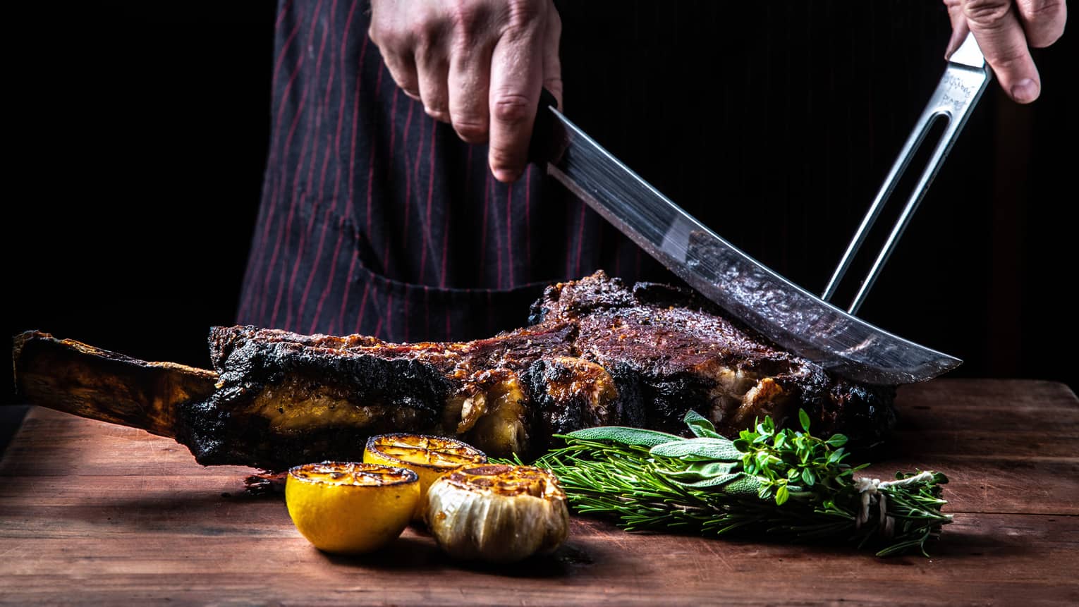 Close-up of chef slicing large rack of grilled meat, vegetables with butcher knives