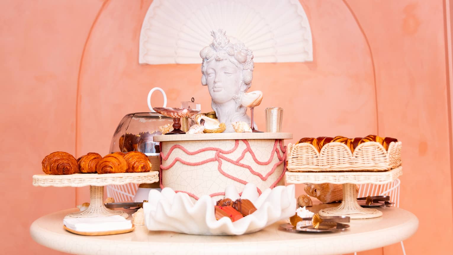 A display of pastries on a round table, with a Roman head of a woman as art