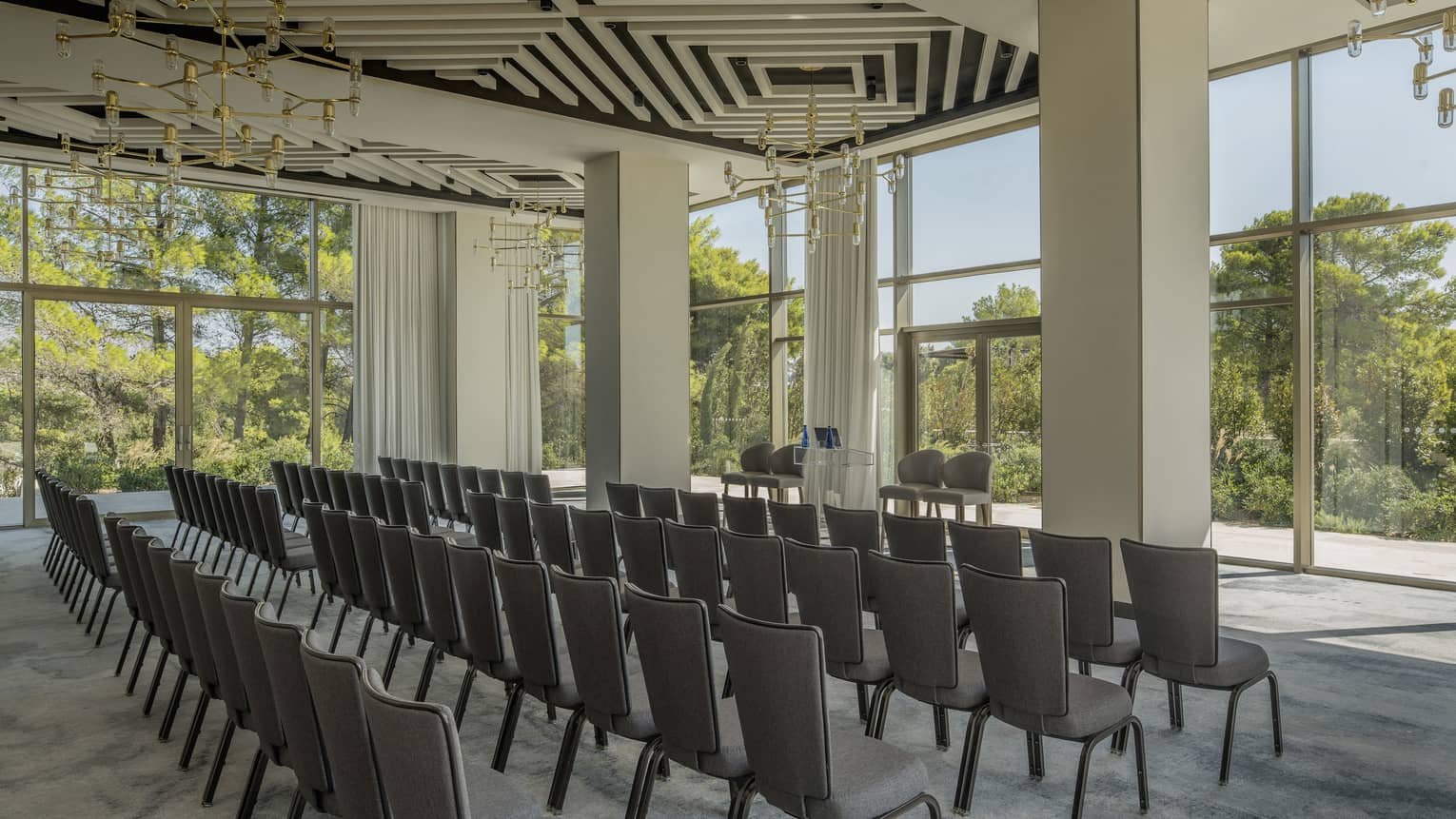Four rows of chairs in light-filled Arion Ballroom with modern light fixtures overlooking trees