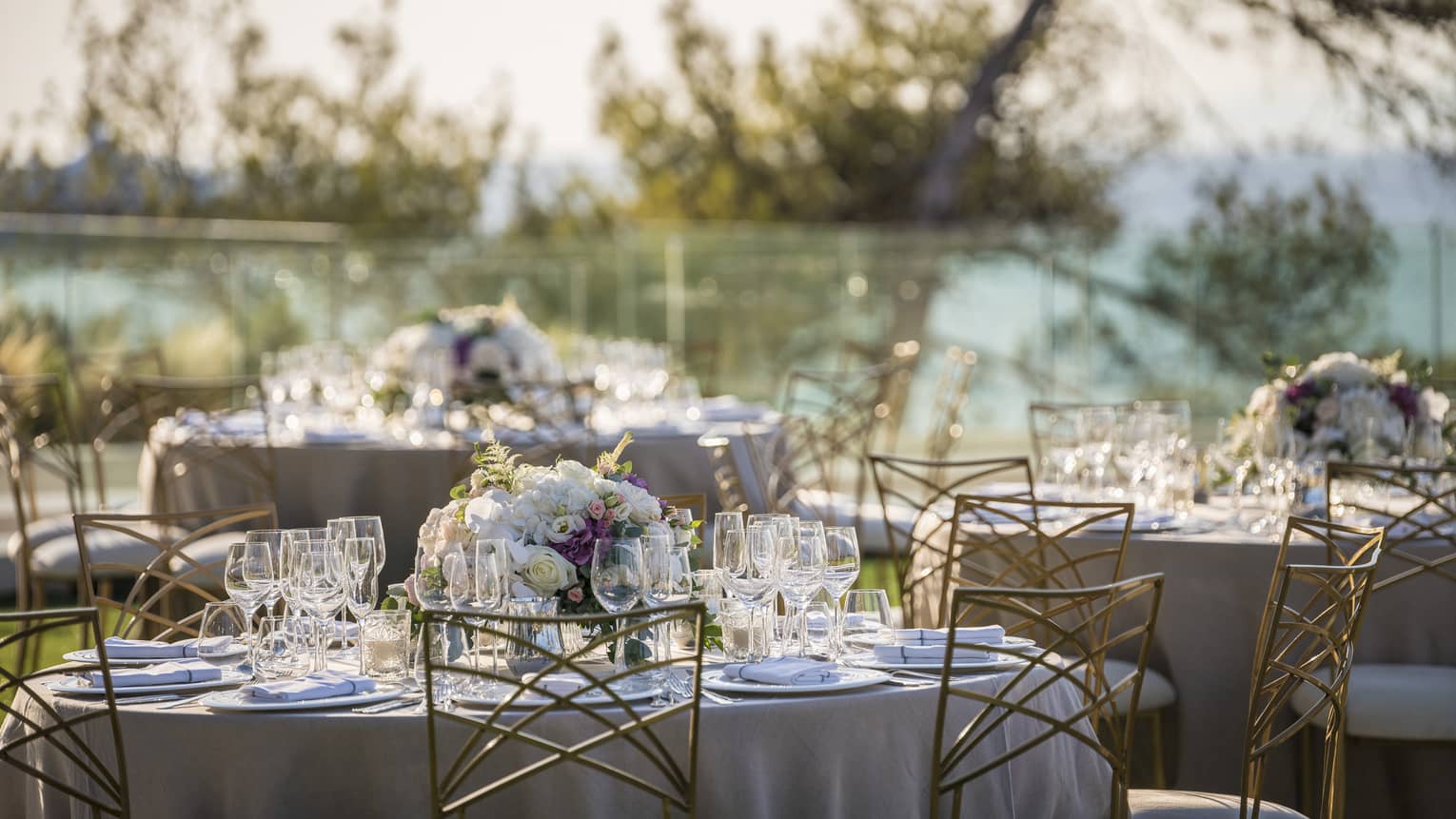 Romantic outdoor table setting with flowers, wine glasses and white linens overlooking trees and ocean