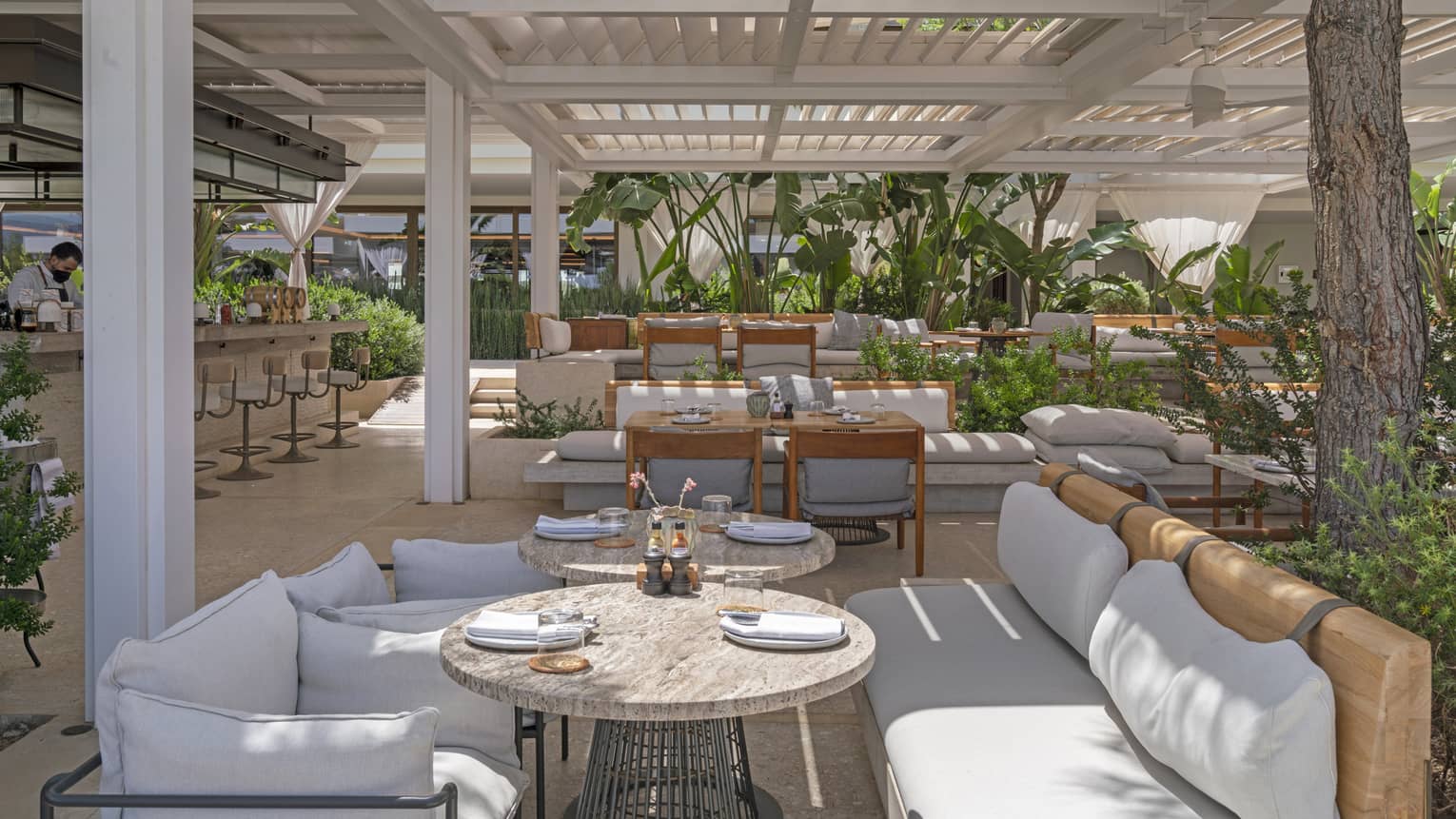 Helios restaurant's terrace with pergola, casual banquette seating, lush greenery and spacious bar