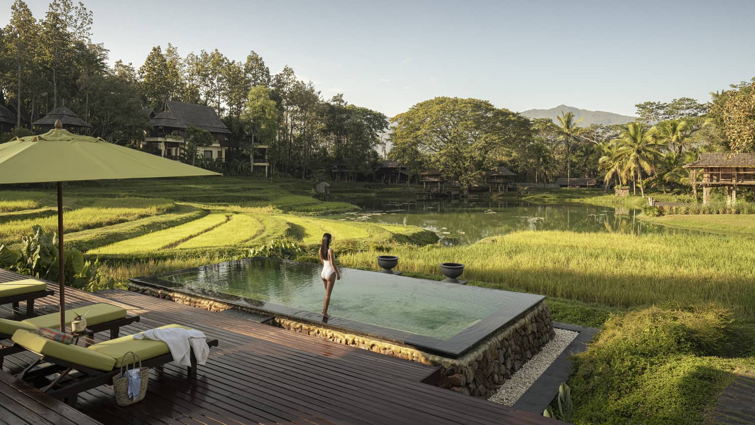 Woman in white bathing suit stands in front of pool overlooking rice paddies