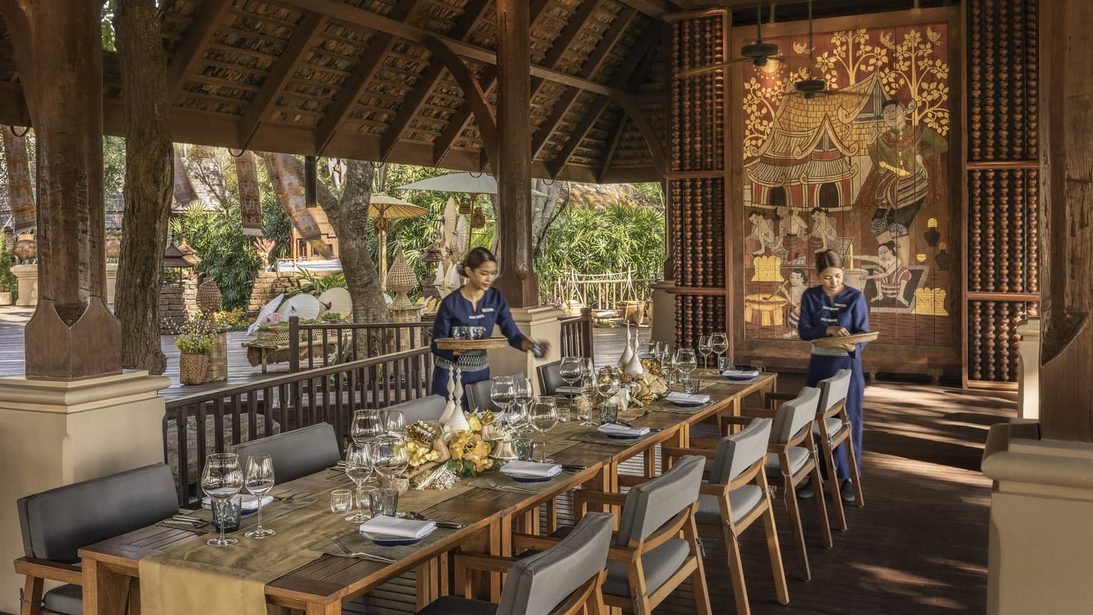 Two waitresses in blue set a long wooden table.