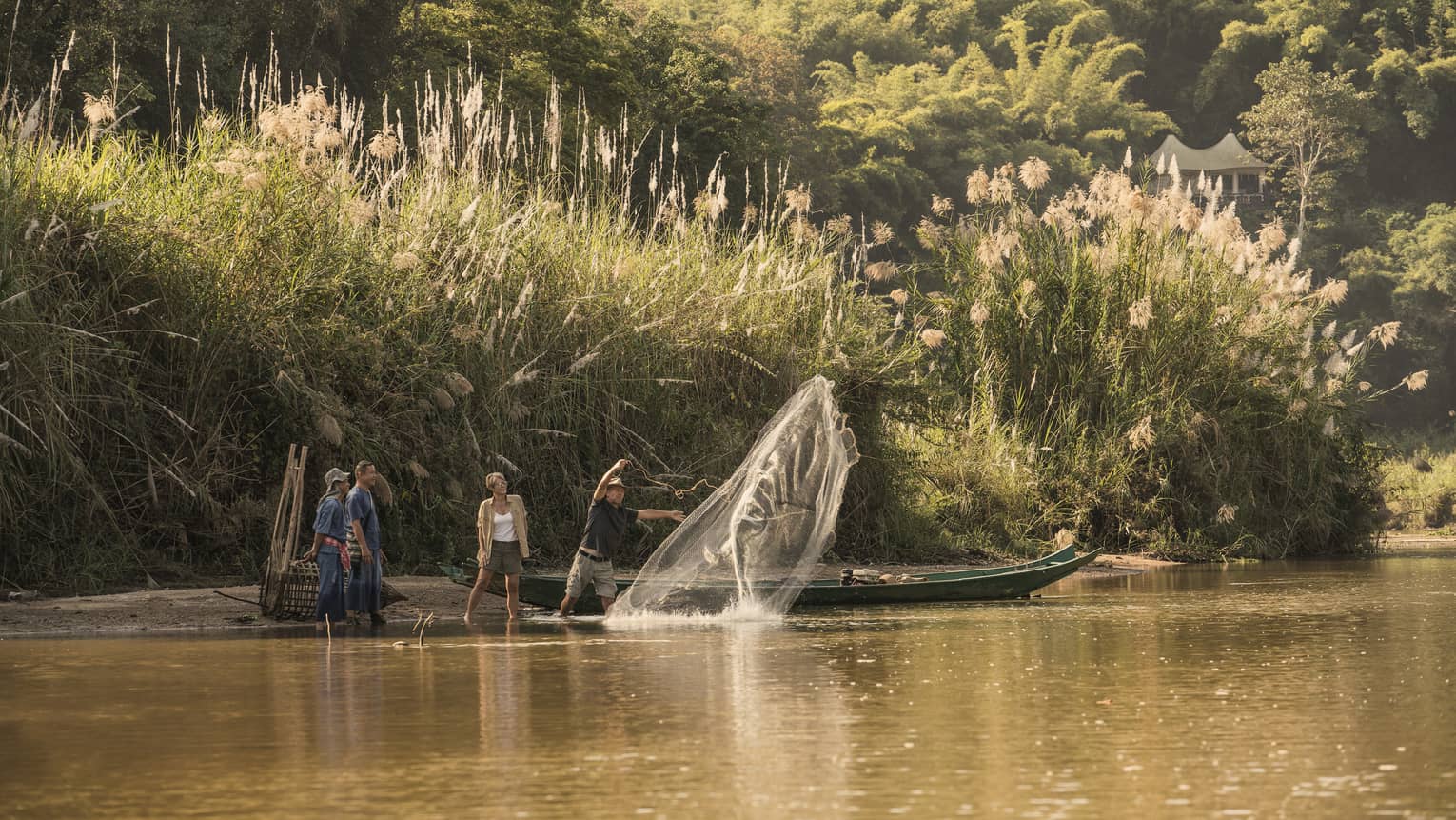 Man throws traditional Thai fishing net from boat into river during group activity