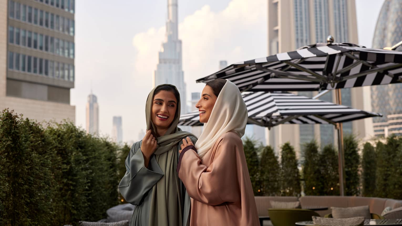 Two women wearing headscarves smile while walking through an outdoor patio