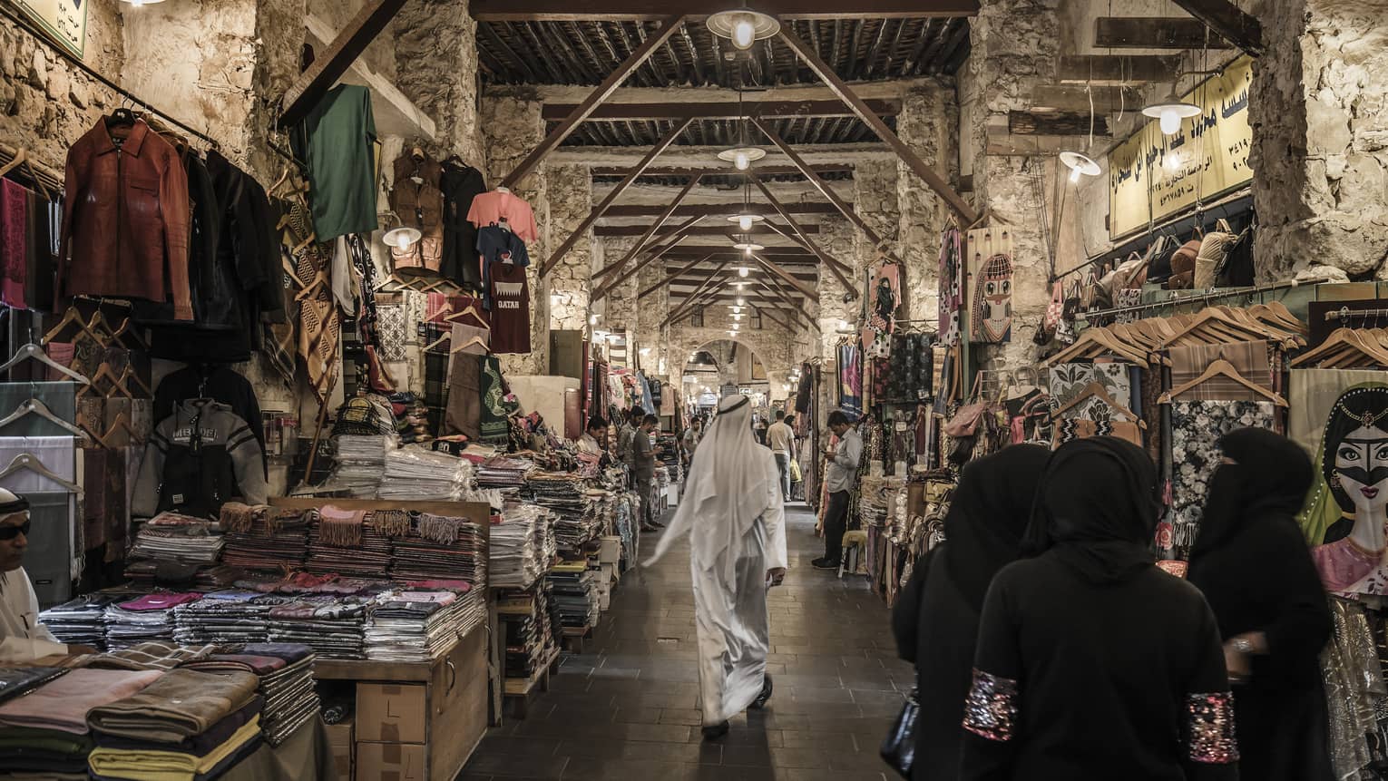 People walk past tables with textiles, clothes in indoor market