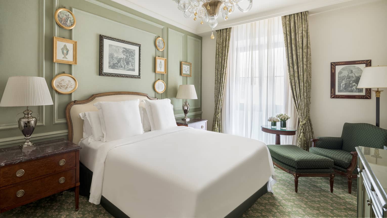 Bedroom with light green walls, small picture frames, crystal chandelier, white king bed