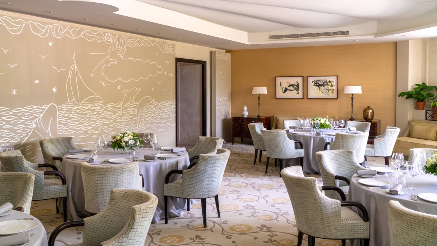 Le Cap restaurant, round set tables, beige rounded chairs, beige sea-themed wall mural