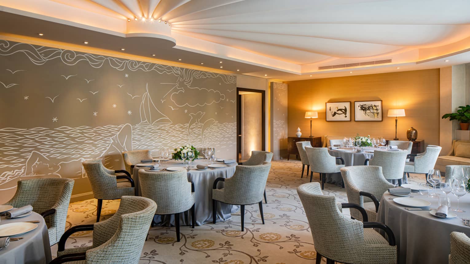 Le Cap restaurant, round set tables, beige rounded chairs, beige sea-themed wall mural, uplit ceiling