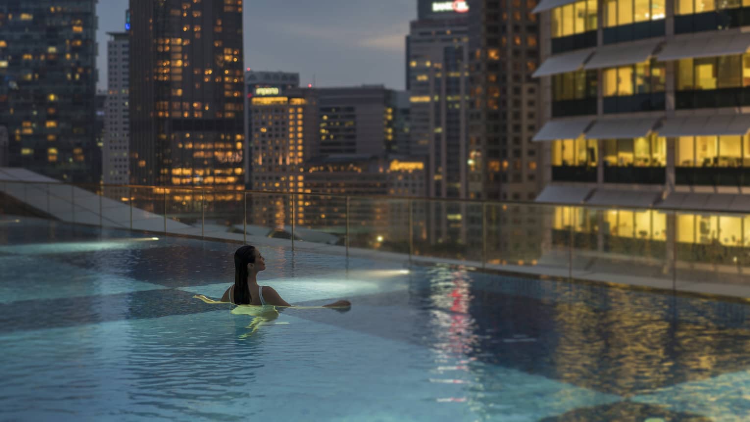 A woman swims in an infinity pool with a view of the city skyline