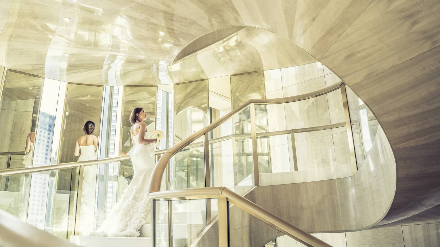 Sun ray illuminate a bride as she walks up a spiral staircase of the white walled hotel 