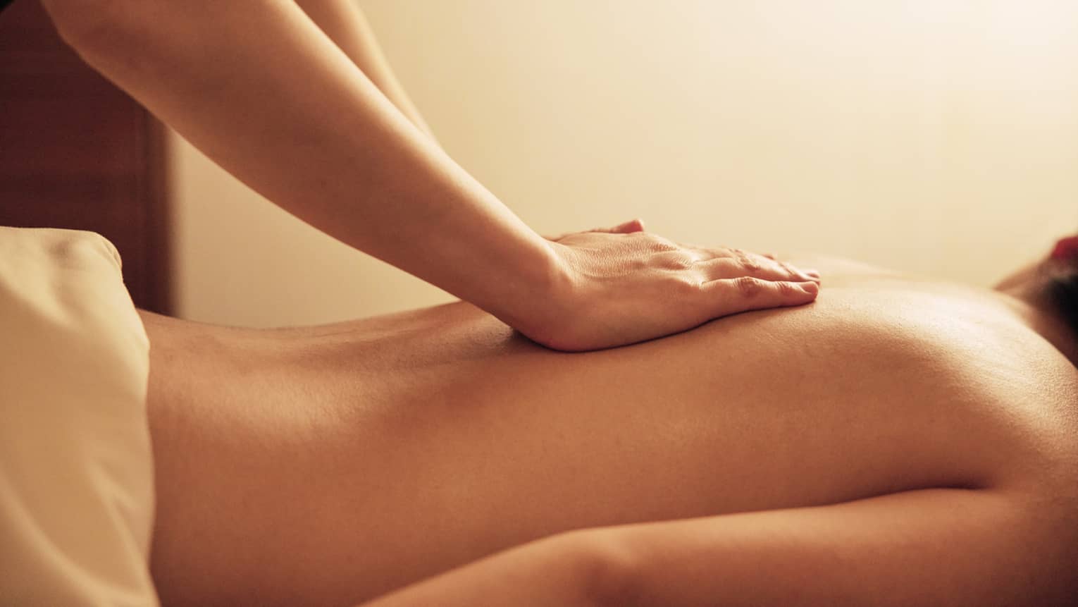 Masseuse rests hands on woman's bare back as she lays on massage table