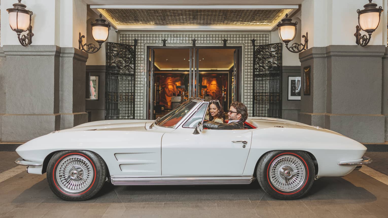 A white car in front of hotel doors.